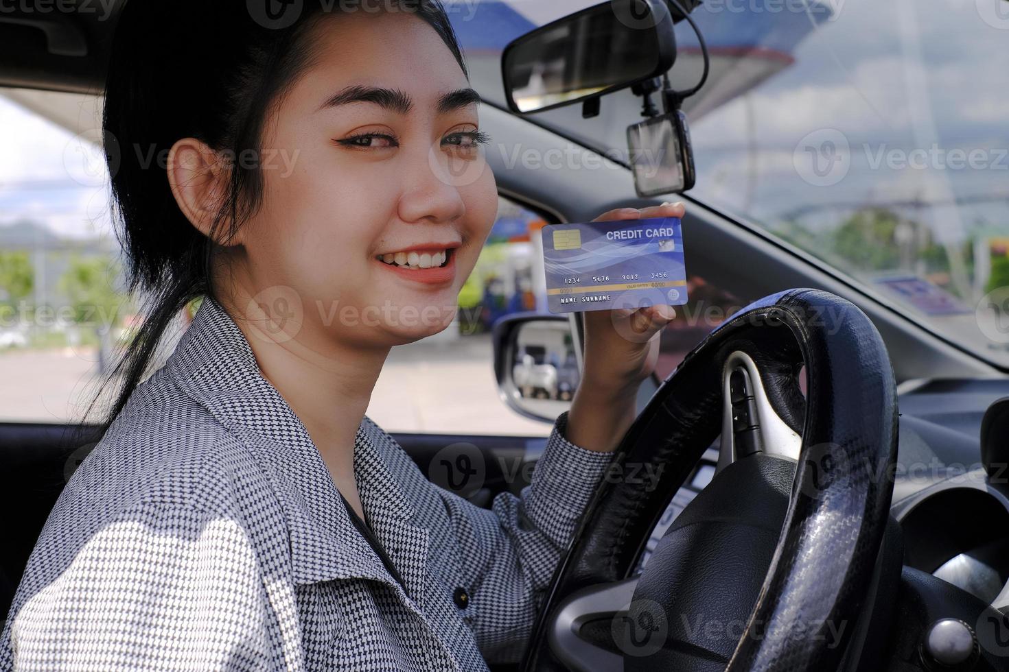 feliz hermosa mujer asiática sentada dentro de su camión mostrando el pago con tarjeta de crédito en una gasolinera foto