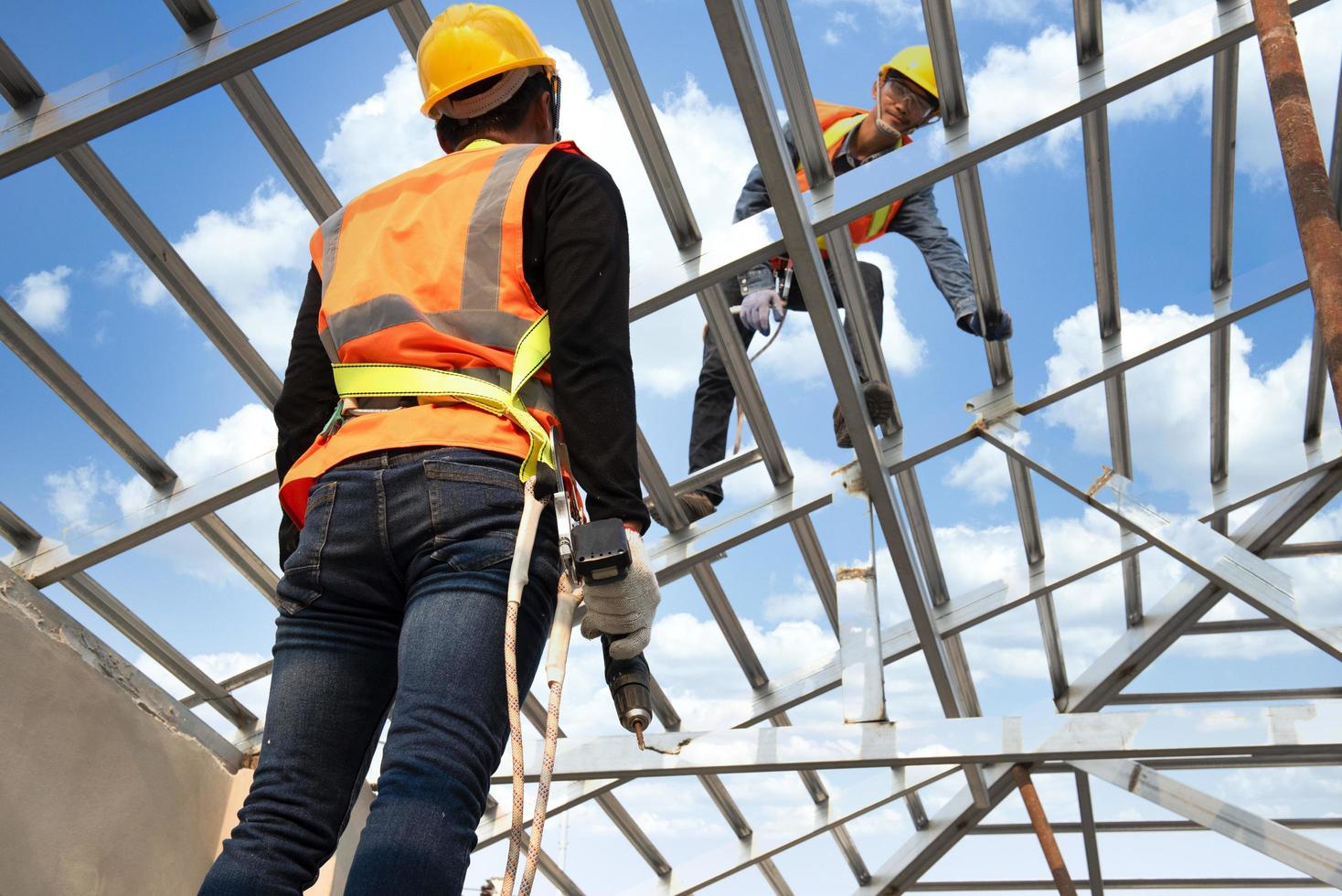 los trabajadores de la construcción usan correas de seguridad mientras trabajan en la estructura del techo del edificio en un sitio de construcción. techador usando una pistola de clavos neumática. foto