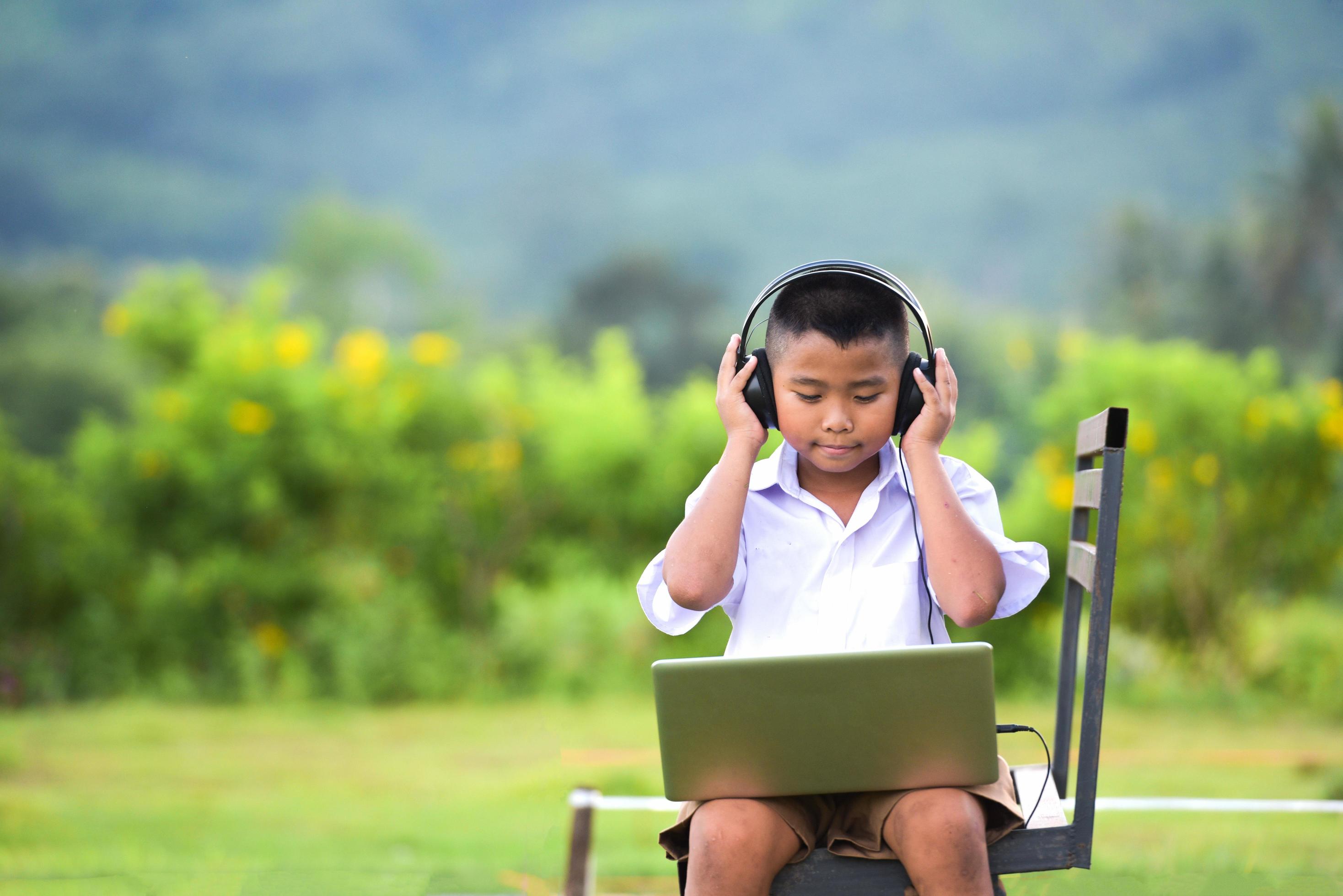 Schoolchildren enjoy listening to music with headphones on the lawn