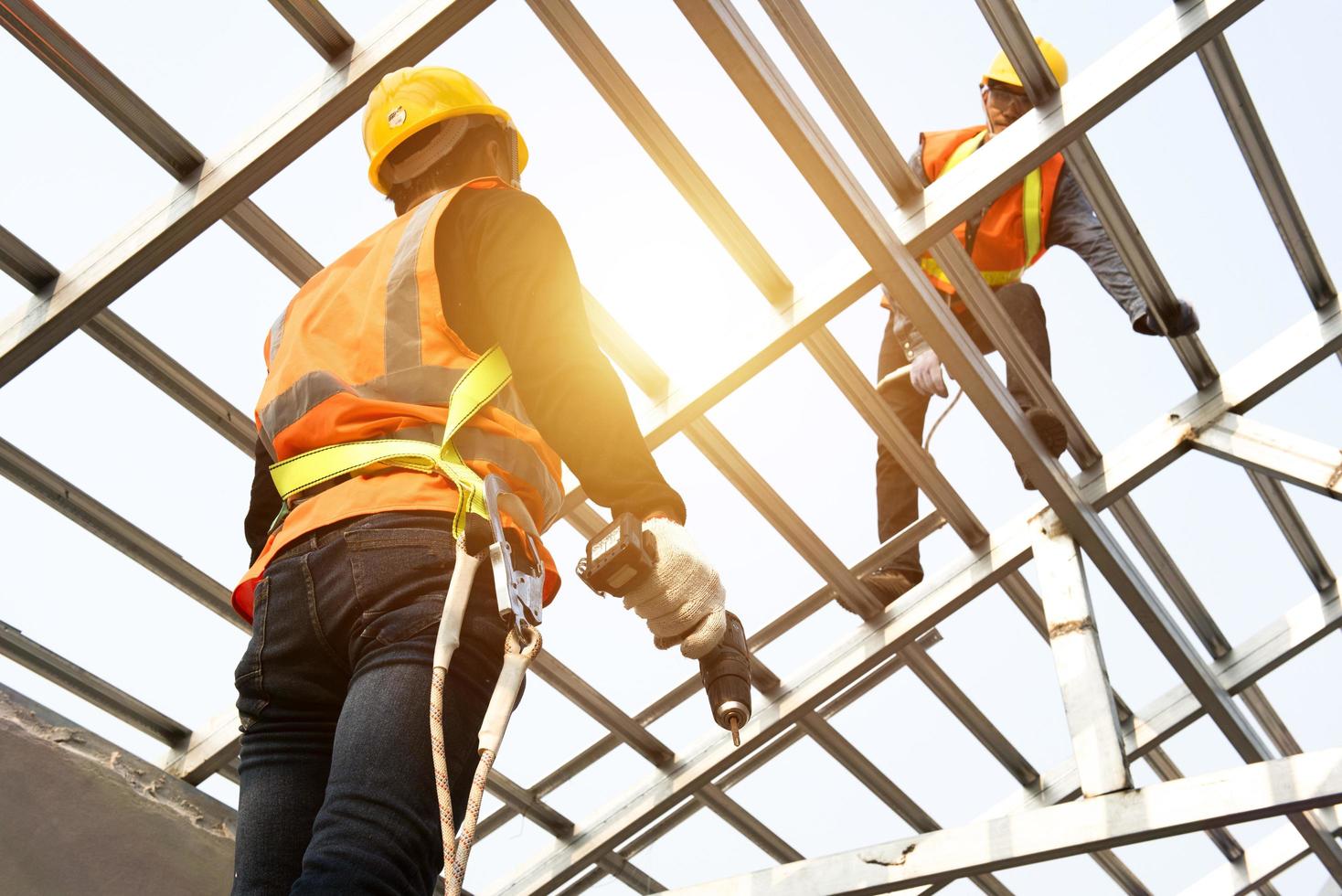 los trabajadores de la construcción usan correas de seguridad mientras trabajan en la estructura del techo del edificio en un sitio de construcción. techador usando una pistola de clavos neumática. foto