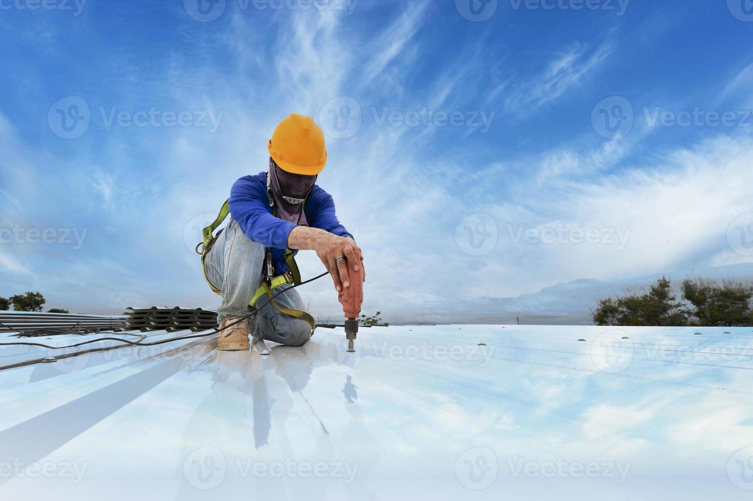 trabajador de la construcción en ropa de trabajo instalando nuevas herramientas para techos herramientas para techos, taladro eléctrico y uso en nuevos techos de madera con láminas de metal. foto