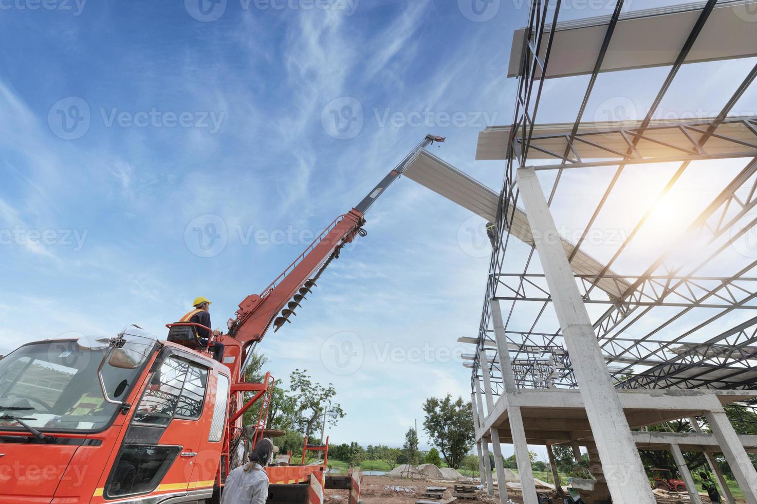 los trabajadores instalan nuevos techos usando grúas móviles. levante la lámina de techo de metal en el marco del techo. subir a la tienda por encima del techo de estructura de acero en el proyecto de construcción. foto