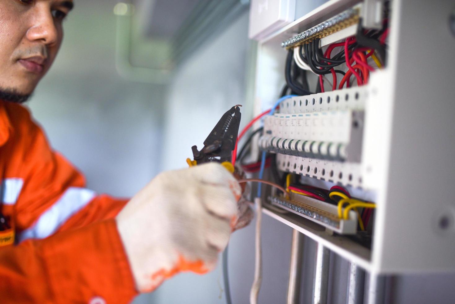 Side view of a handsome Asian electrician repairing an electrical box with pliers in the corridor. photo