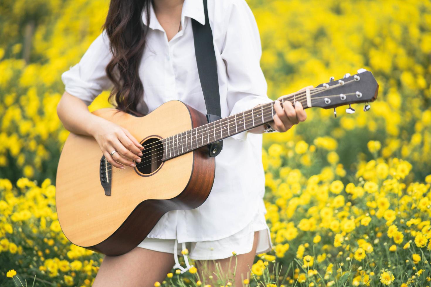 mujer joven asiática tocando la guitarra y cantando música en el parque, mujer asiática tocando la guitarra en el jardín de flores amarillas foto