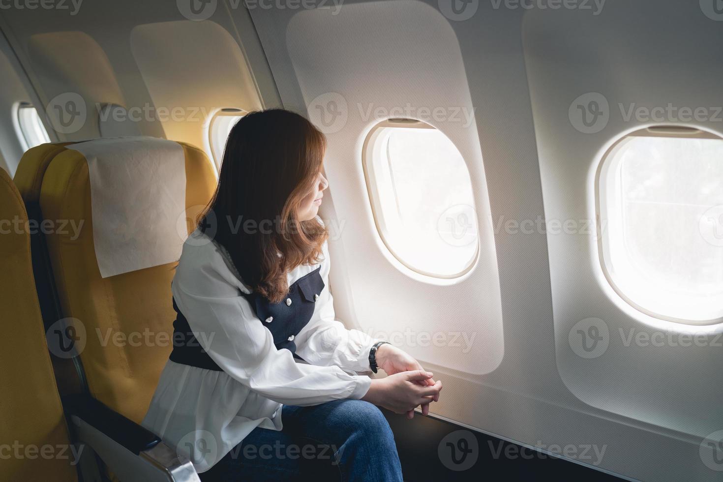 Asian woman sitting in a seat in airplane and looking out the window going on a trip, asian woman passenger is leaving for a trip by plane on vacation. Vacation travel concept. photo