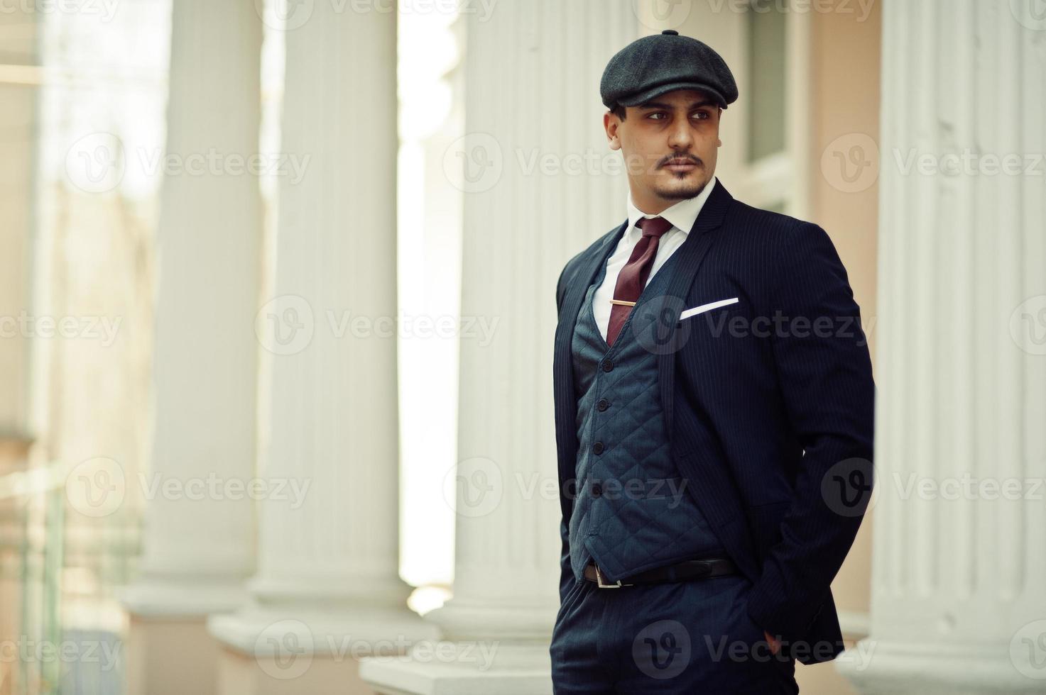 Portrait of retro 1920s english arabian business man wearing dark suit, tie and flat cap. photo