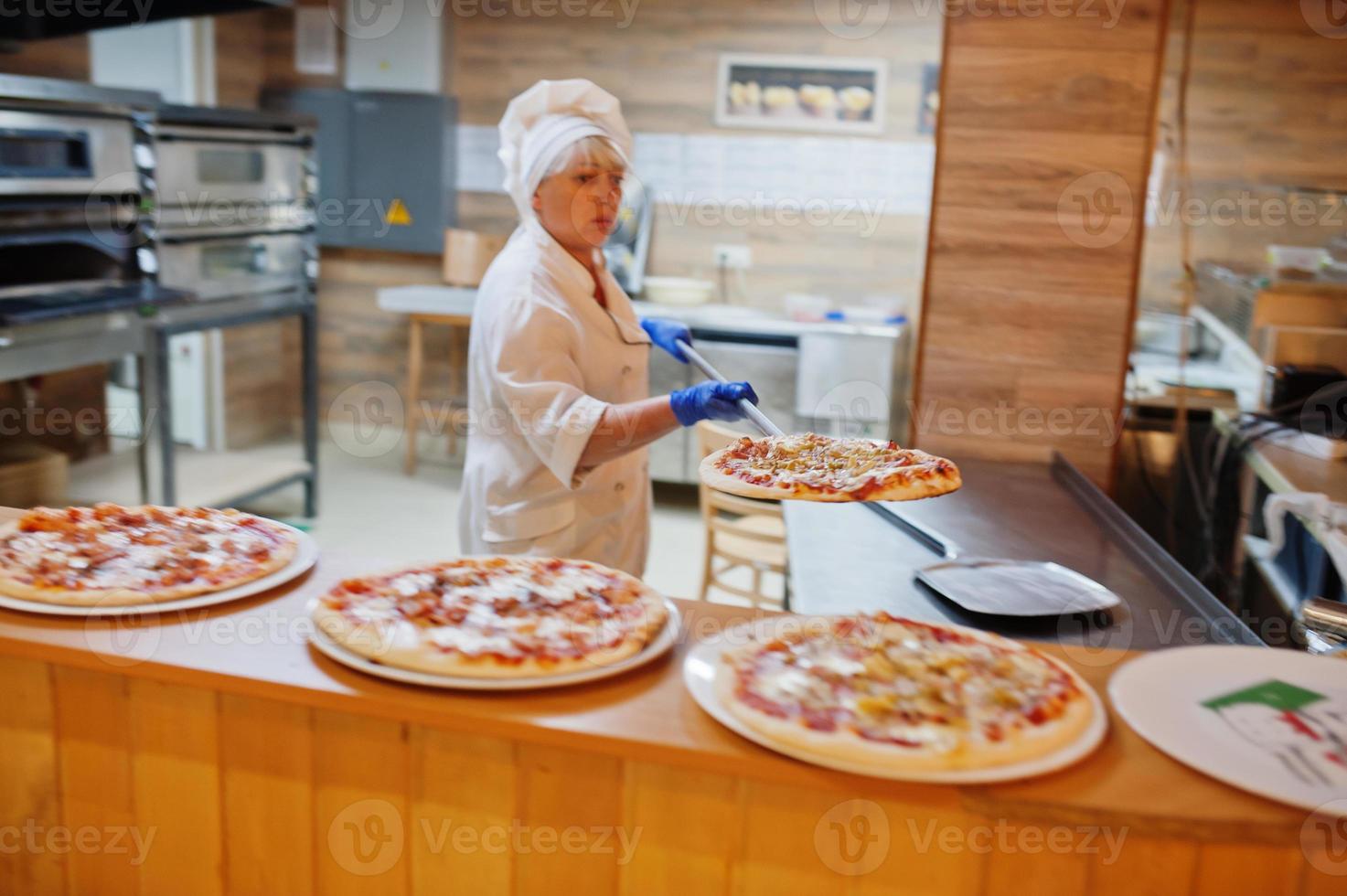 Female chef preparing pizza in restaurant kitchen. photo