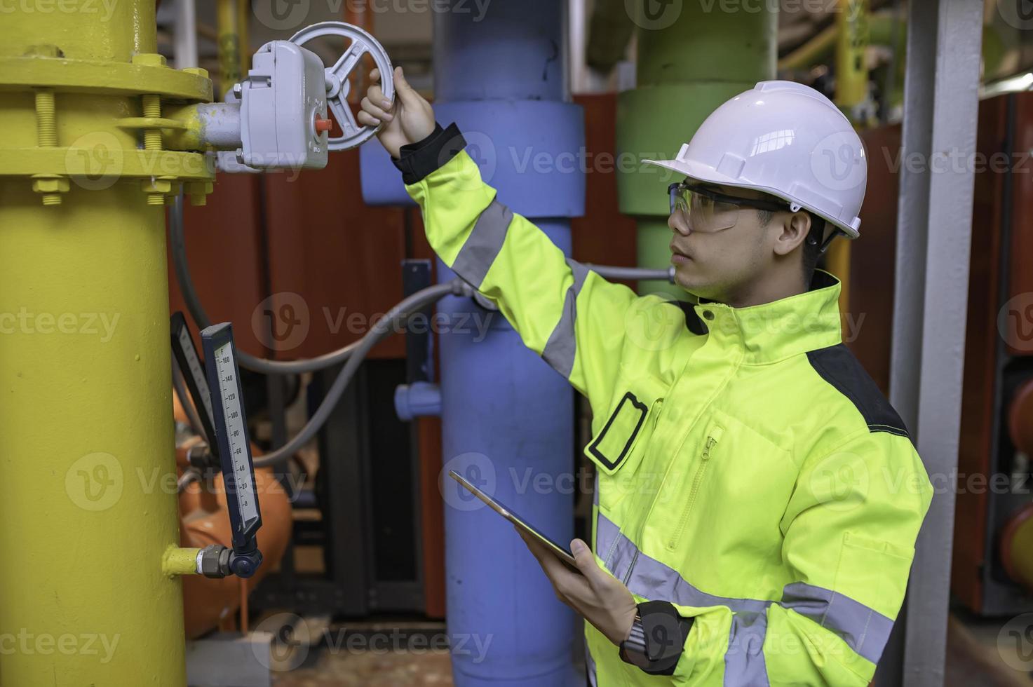 Asian engineer wearing glasses working in the boiler room,maintenance checking technical data of heating system equipment,Thailand people photo