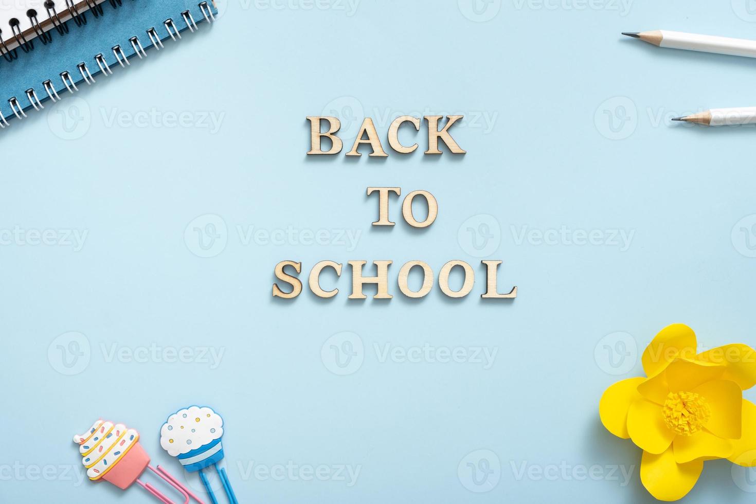 Office desk with Back to school text from wooden letters. Flat lay. Notebook, note, pencils, paper clip, on pastel blue background photo