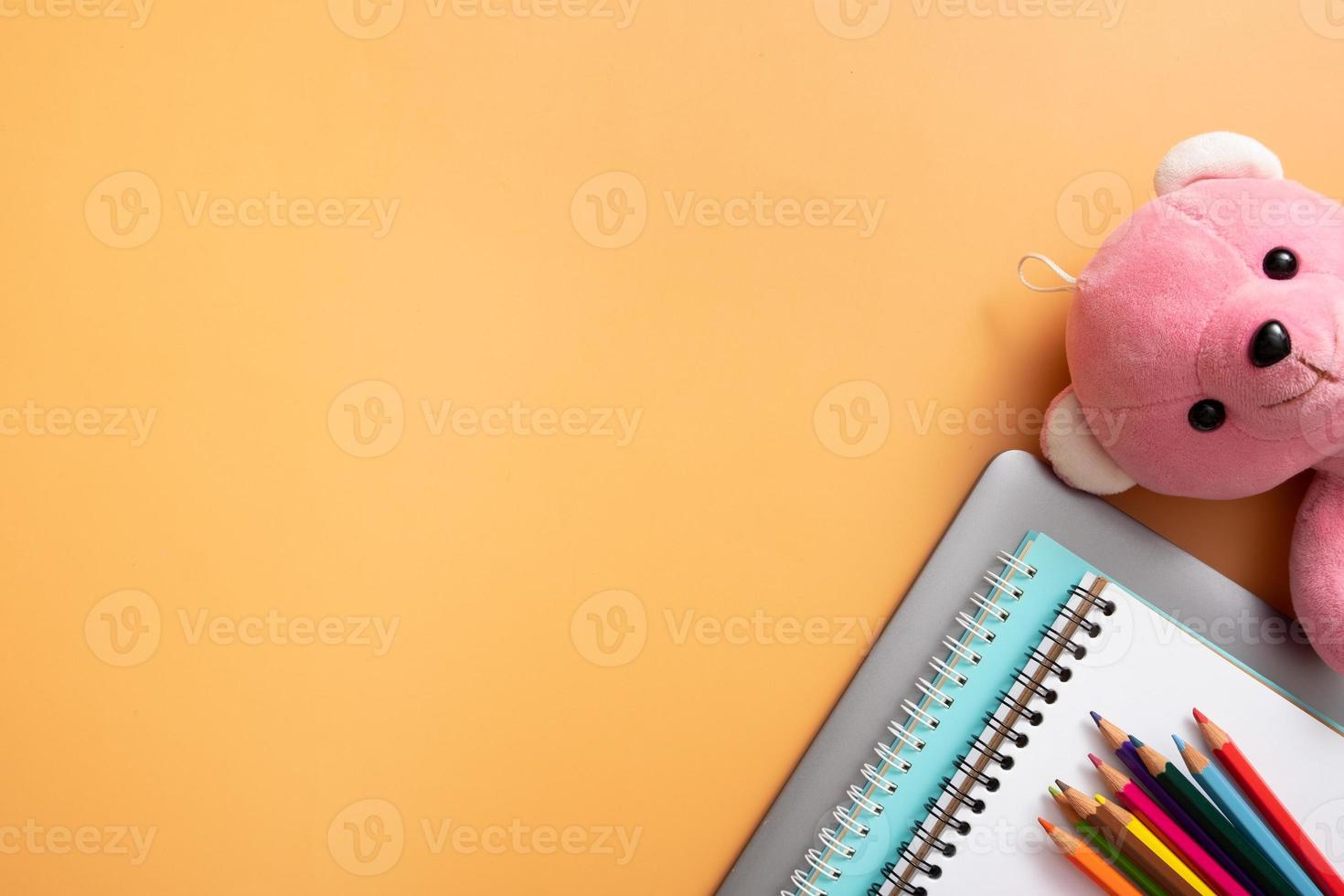 Stationary and laptop with teddy bear on colored background. Copy space. Kids work space top view, flat lay. Online learning concept photo