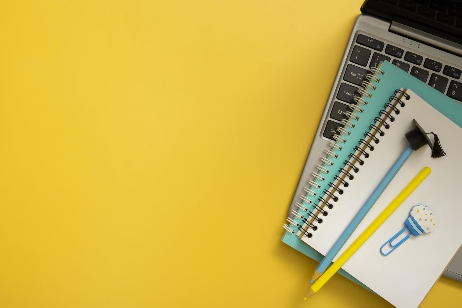 Colorful pencils with graduated cap and note on laptop on colored background. Copy space. Children work space top view, flat lay photo