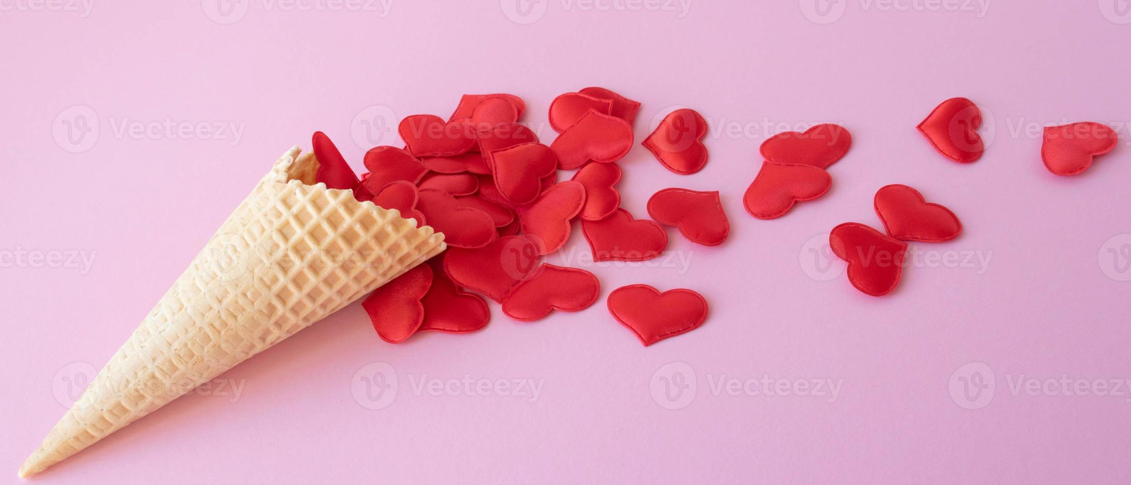 Creative photo of empty waffle cones with scattered red hearts on a pink background. The concept of love, summer, spring