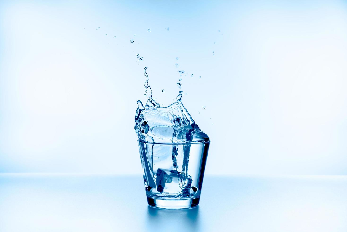 Ice that fell into the glass with water splashing from glass isolated on blue background photo