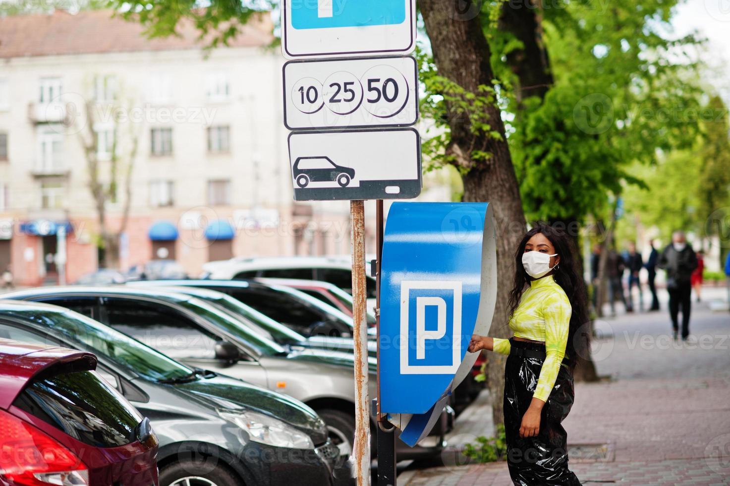 African American woman posing with facial mask to protect from infections from bacteria, viruses and epidemics, using parking pay station terminal. photo