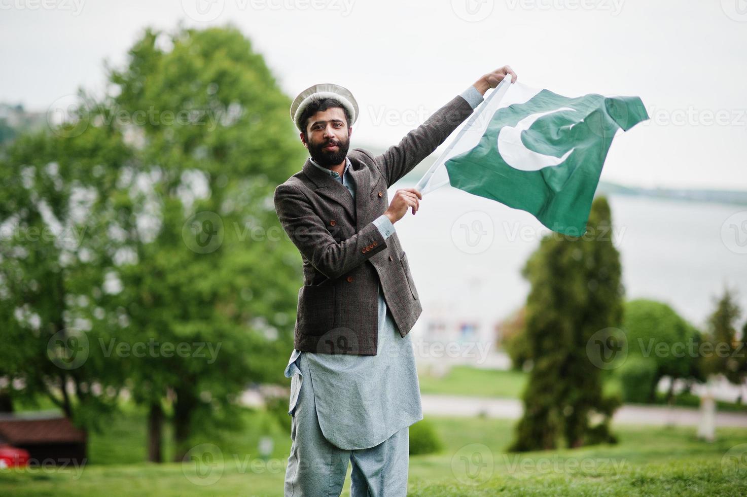El hombre pakistaní de barba usa sombrero pakol y chaqueta sostiene la bandera de pakistán. foto