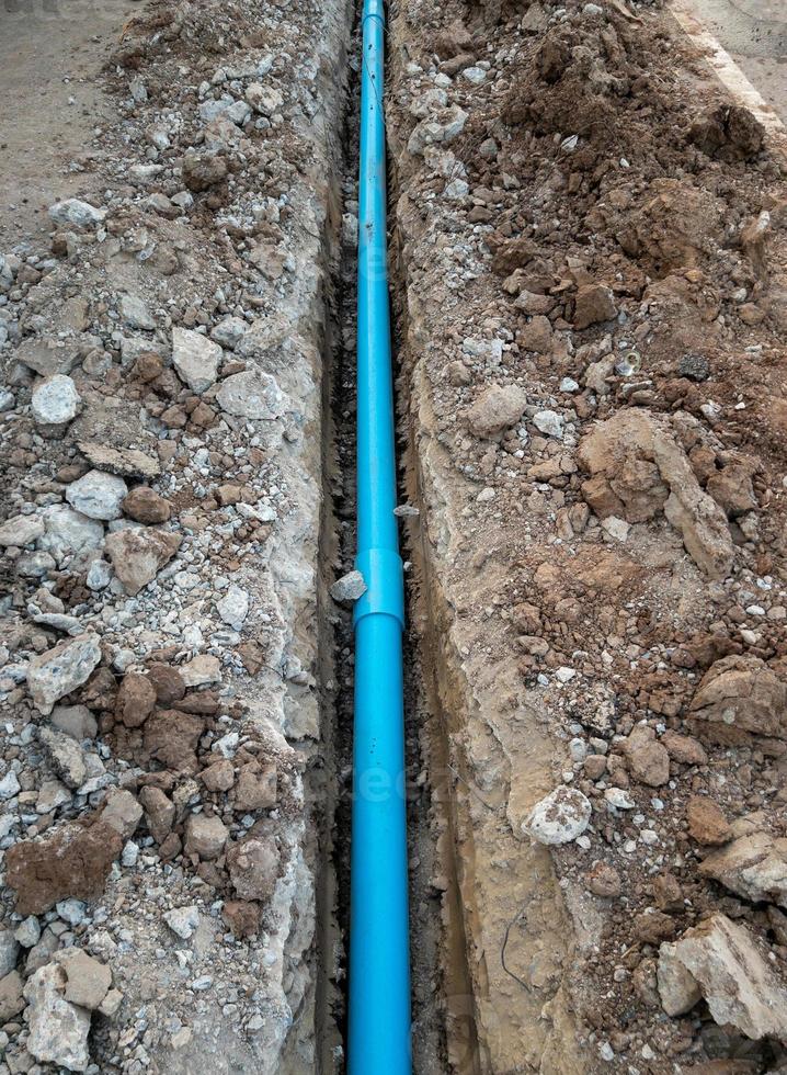 The new PVC pipe is laying in the trench near the asphalt road. photo