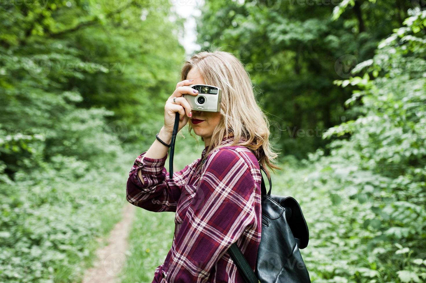 Portrait of a gorgeous young girl in tartan shirt taking pictures with camera in the forest. photo