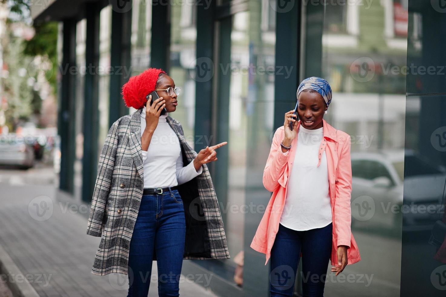 Two young modern fashionable, attractive, tall and slim african muslim womans in hijab or turban head scarf and coat posed with mobile phones. photo