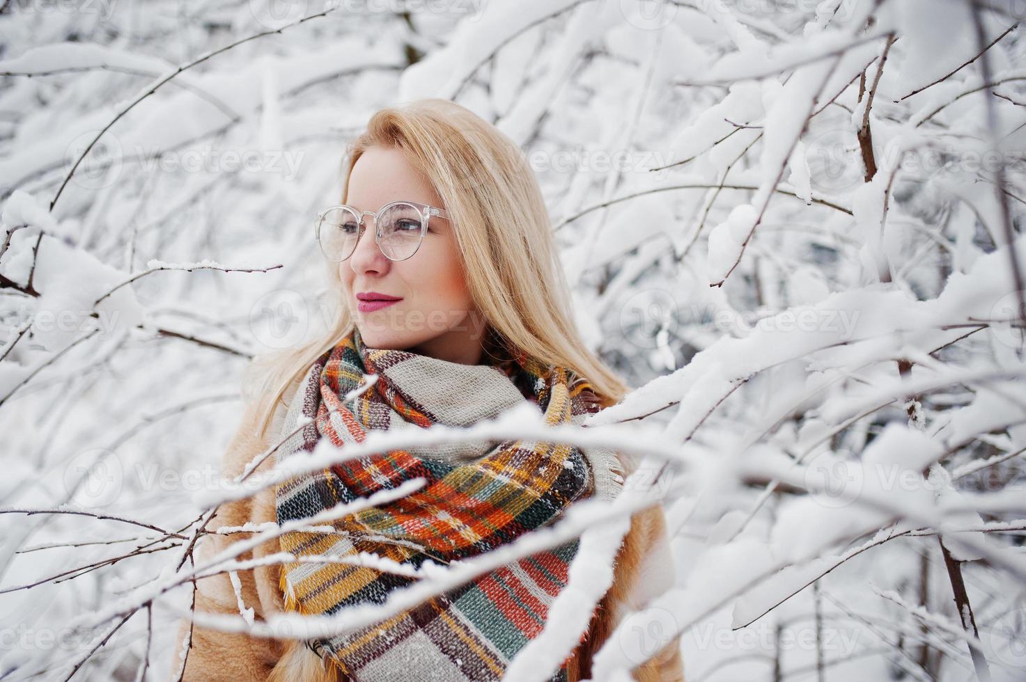 Portraiy of blonde girl in glasses, red fur coat and scarf at winter day. photo