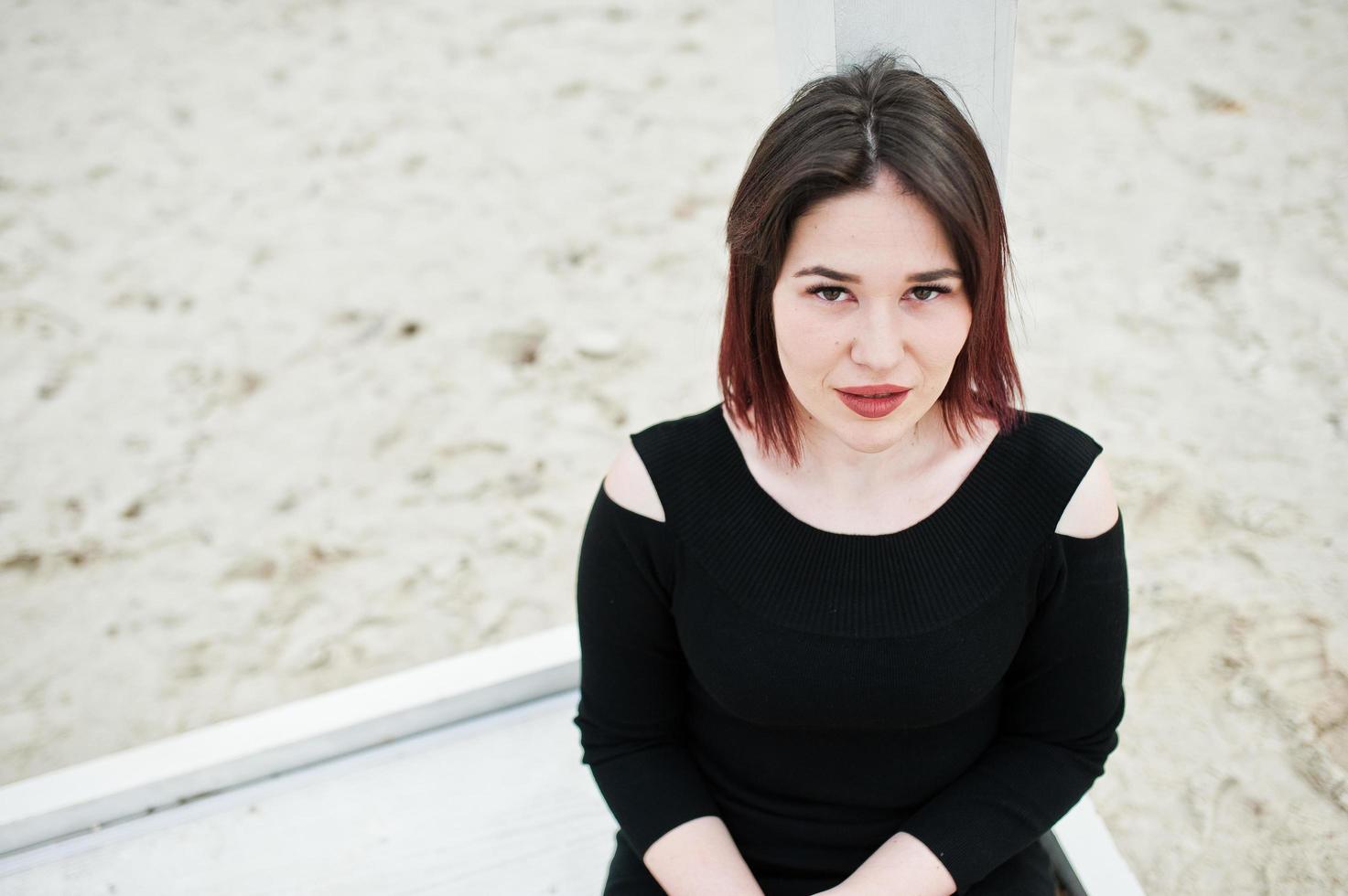 Portrait of brunette girl in black dress sitting at white wooden construction. photo