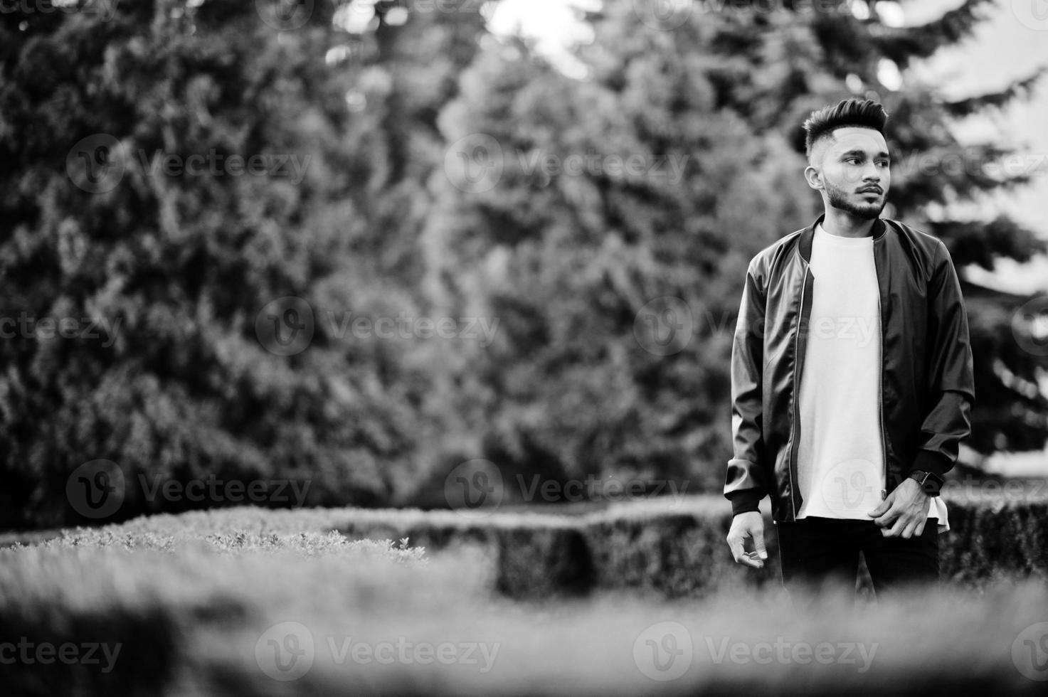 Stylish indian beard man at black leather jacket. India model posed at green garden of city. photo