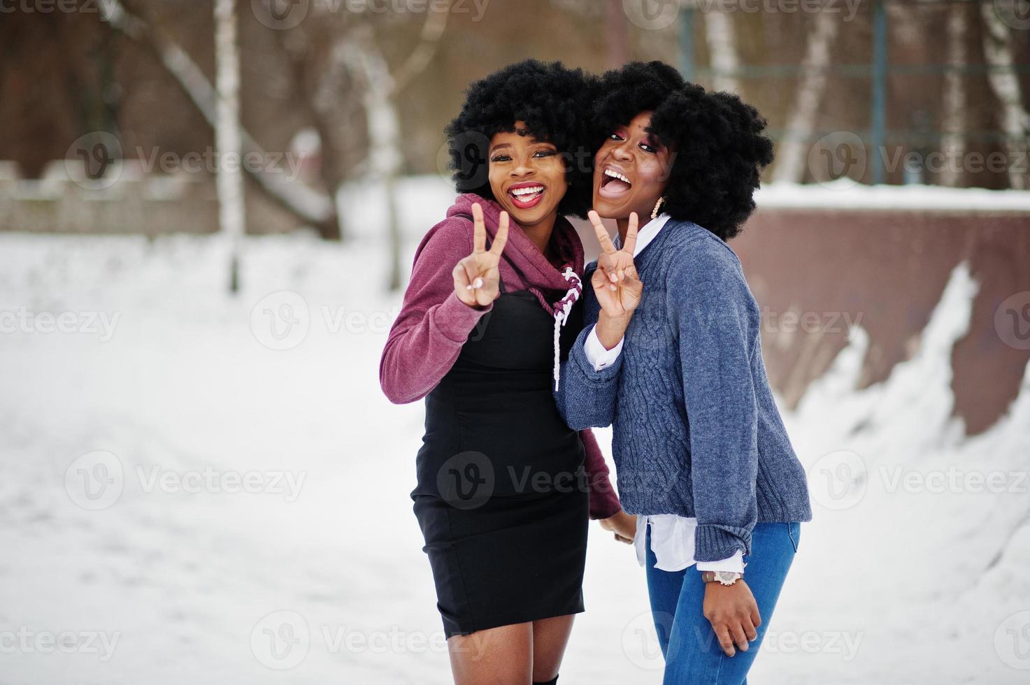 Two curly hair african american woman wear on sweaters posed at winter day, show two fingers. photo