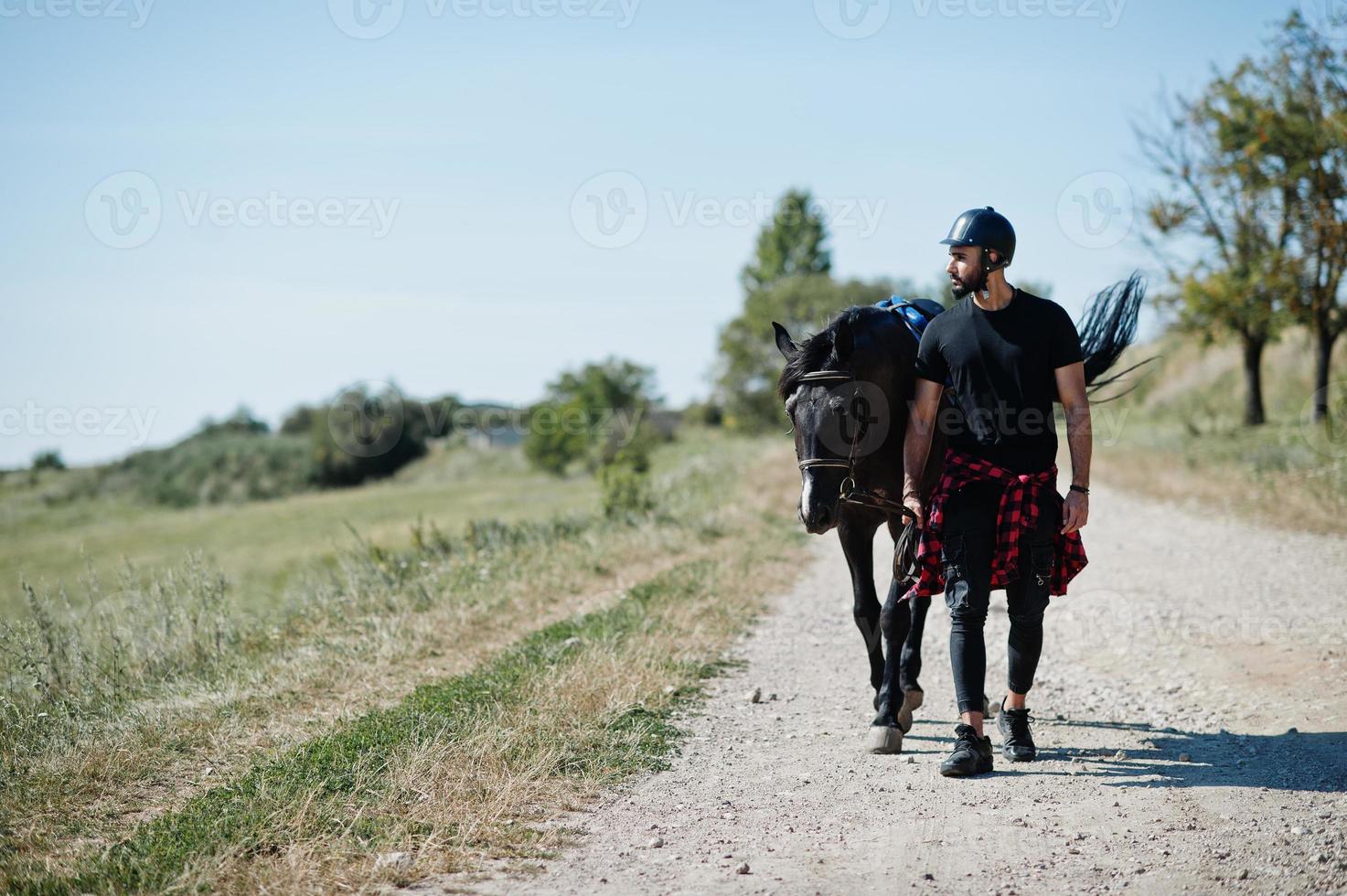 El hombre árabe de barba alta usa casco negro con caballo árabe. foto