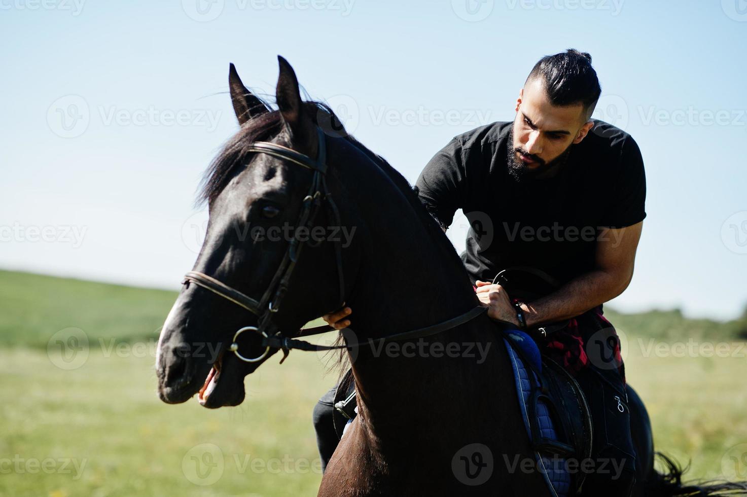 El hombre árabe de barba alta usa un caballo árabe negro. foto