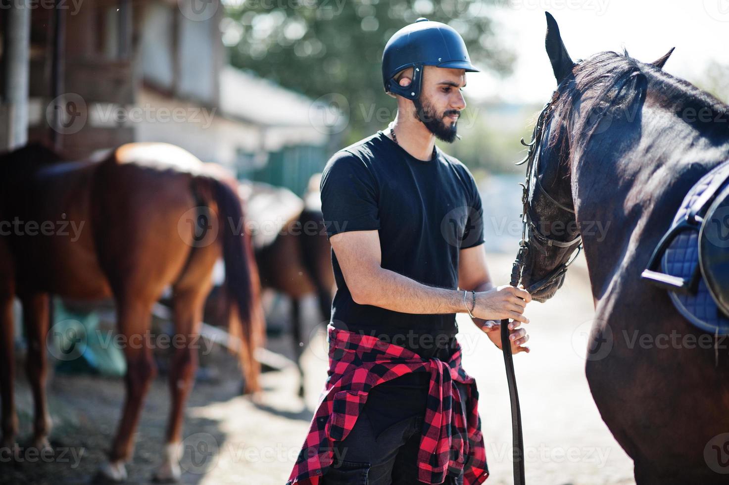 El hombre árabe de barba alta usa casco negro con caballo árabe. foto