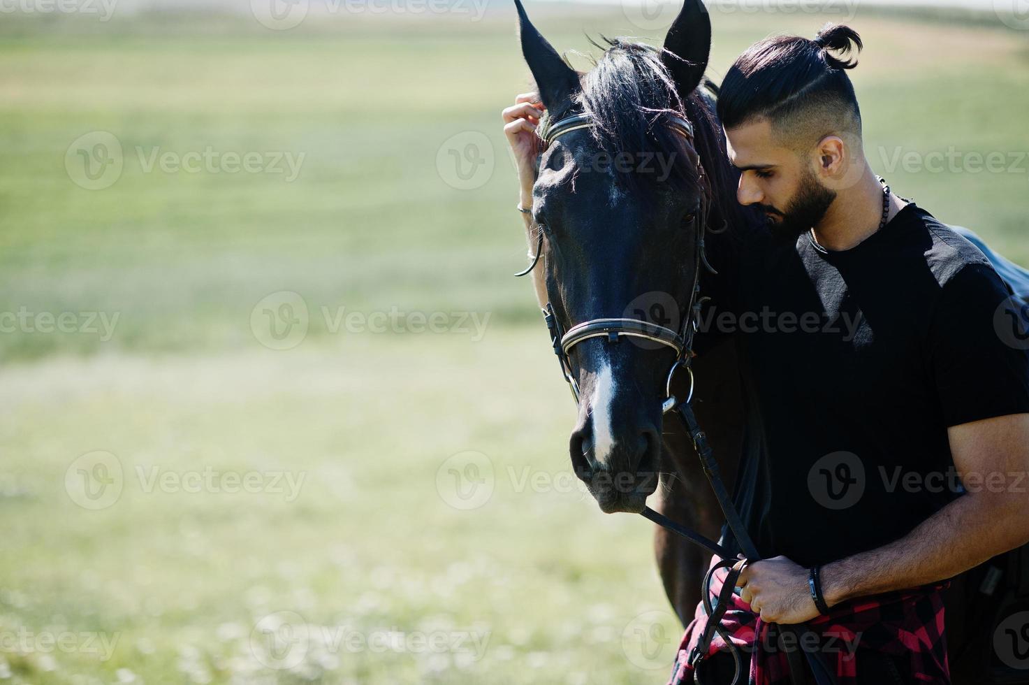 Hombre árabe de barba alta vestido de negro con caballo árabe. foto