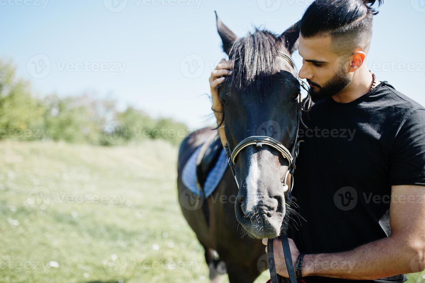 Hombre árabe de barba alta vestido de negro con caballo árabe. foto