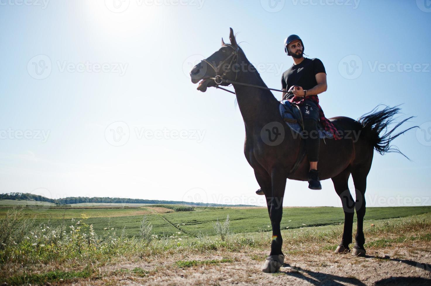 El hombre árabe de barba alta usa casco negro, monta un caballo árabe. foto