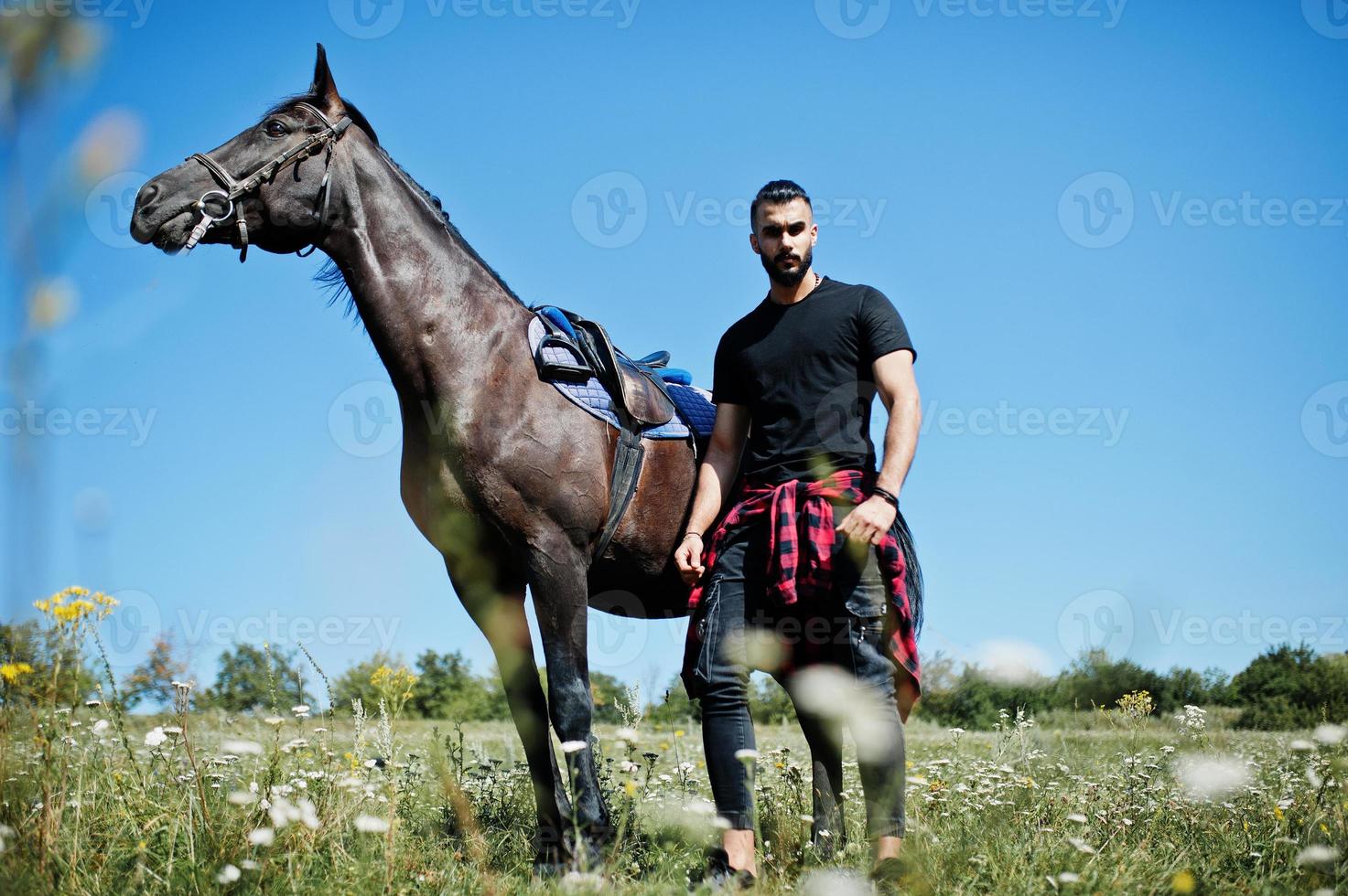 Hombre árabe de barba alta vestido de negro con caballo árabe. foto