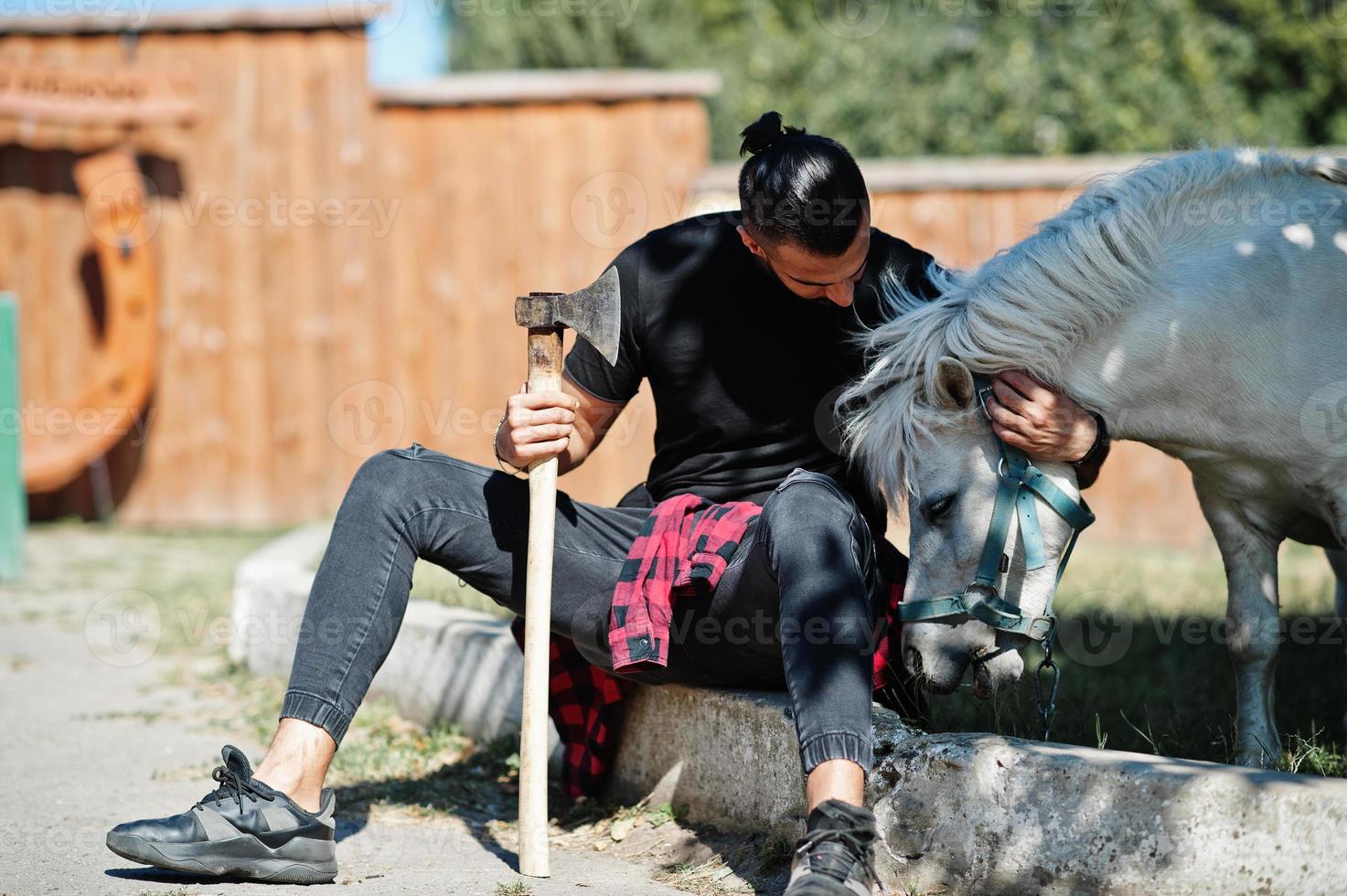 Arab hipster beard man lumberjack hold axe against pony horse. photo