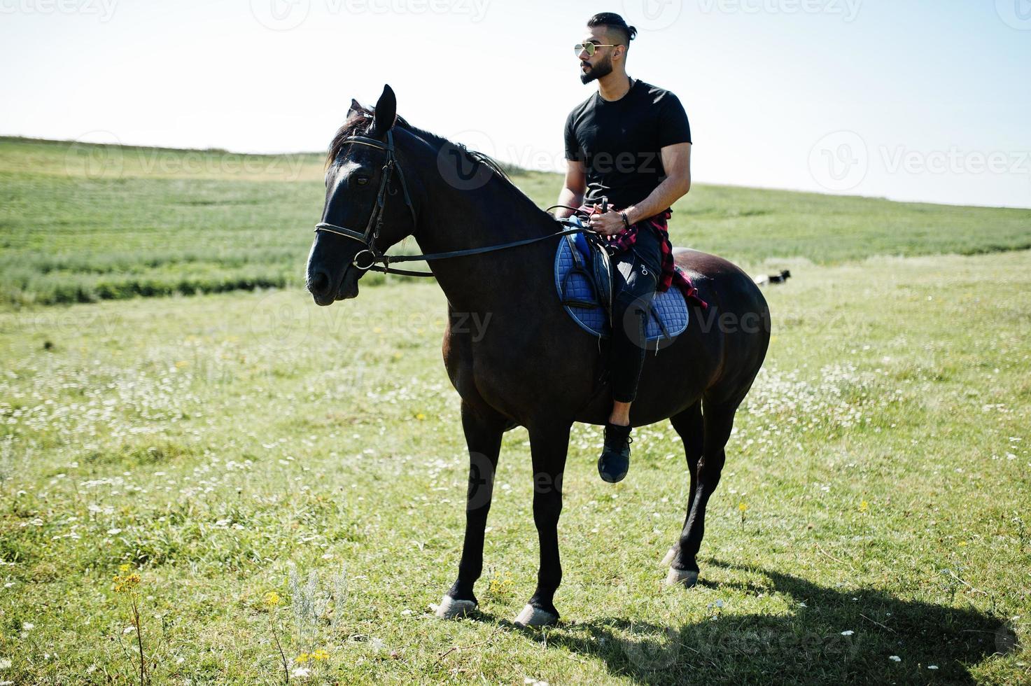 Arab tall beard man wear in black and sunglasses ride arabian horse. photo