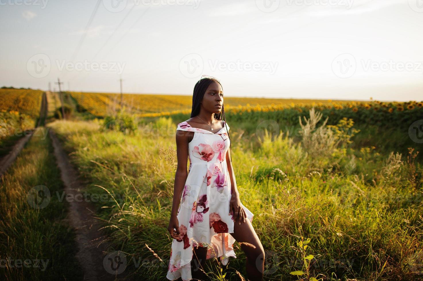 una mujer negra muy joven usa una pose de vestido de verano en un campo de girasoles. foto