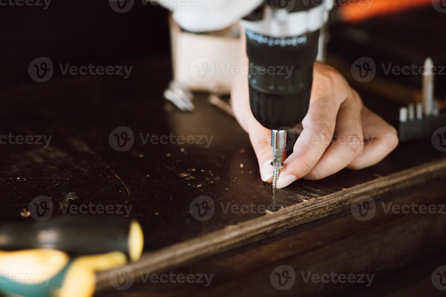 Close up of male mechanic holding electric cordless screwdriver drill with wood screw in the factory. Working with the screw. Professional carpenter. Concept furniture at home. photo