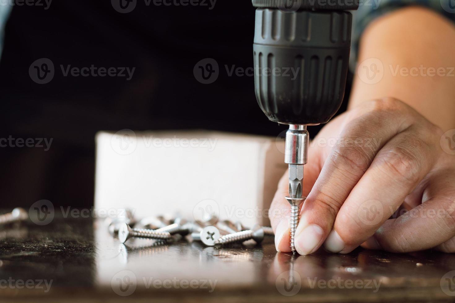 Close up of male mechanic holding electric cordless screwdriver drill with wood screw in the factory. Working with the screw. Professional carpenter. Concept furniture at home. photo