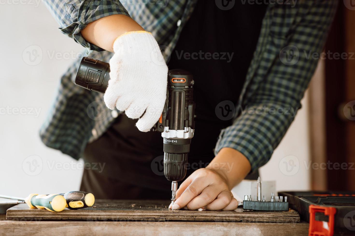 Close up of male mechanic holding electric cordless screwdriver drill with wood screw in the factory. Working with the screw. Professional carpenter. Concept furniture at home. photo