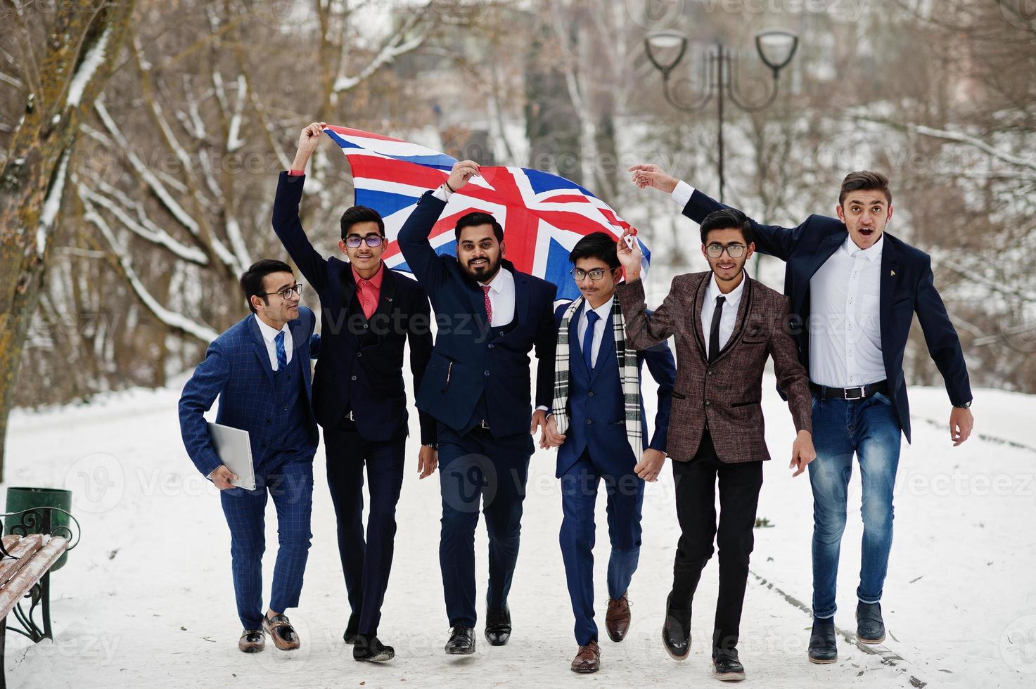 grupo de seis hombres de negocios indios en trajes posados al aire libre en un día de invierno en europa con bandera de gran bretaña. relaciones amistosas con la india y el reino unido. foto