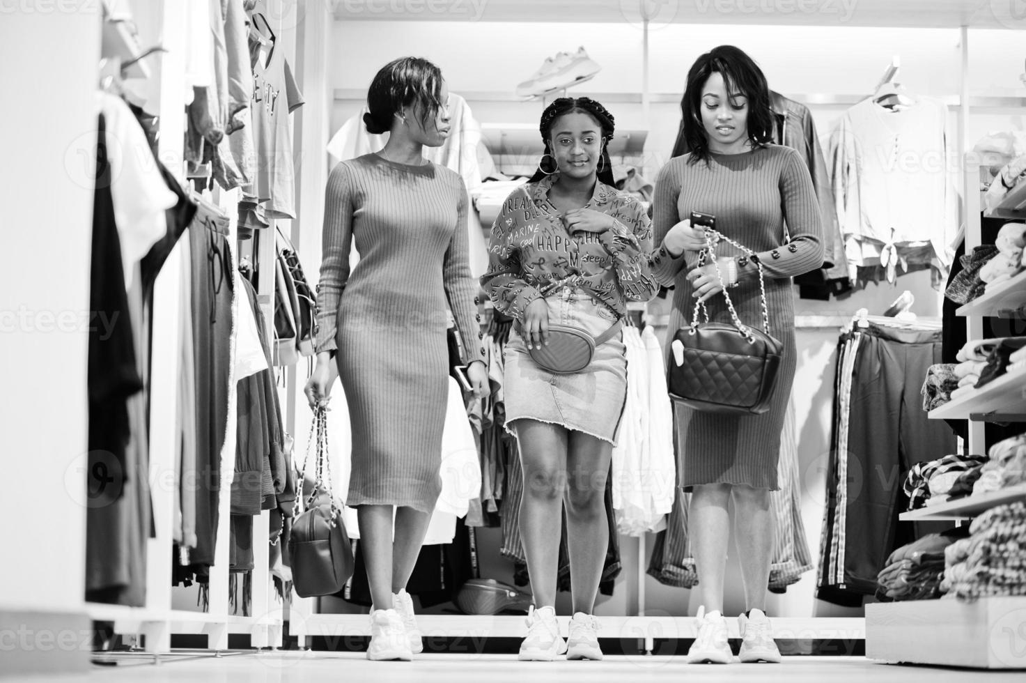 Three attractive african american woman in brown tunic dress posed at clothes store with handbags. It's time for shopping. photo