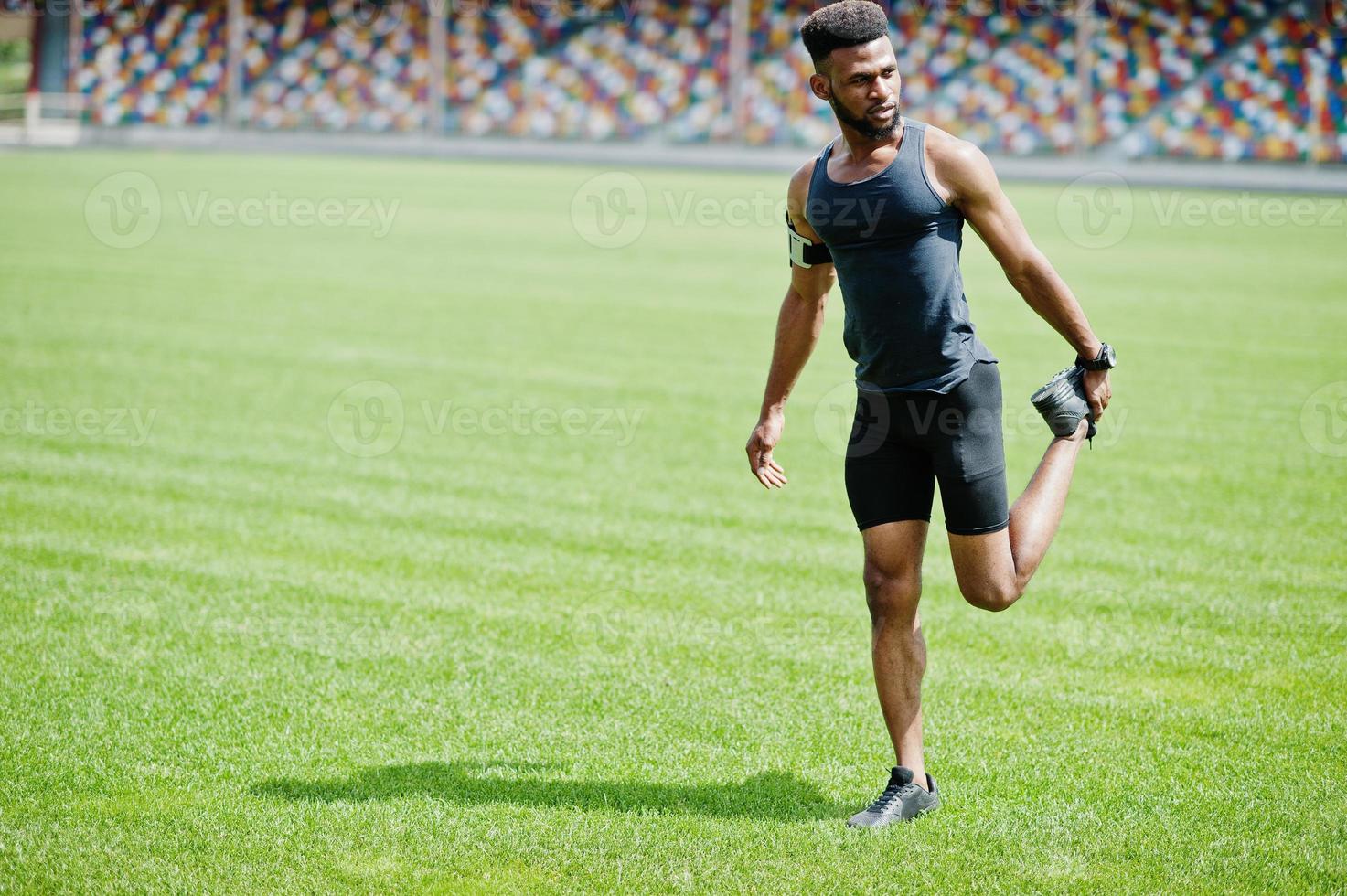 African american male athlete in sportswear doing stretching exercise at stadium. photo