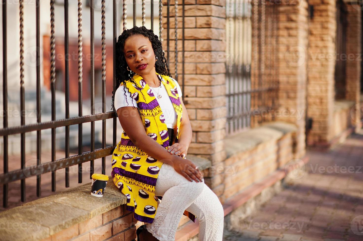 Stylish african american women in yellow jacket posed on street with hot drink in disposable paper cup. photo