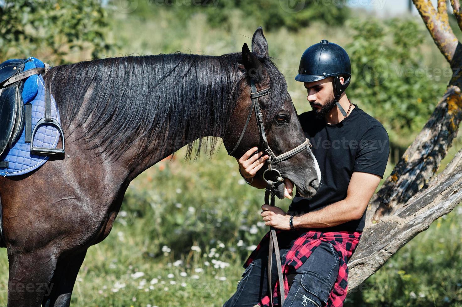 Arab tall beard man wear in black helmet with arabian horse. photo