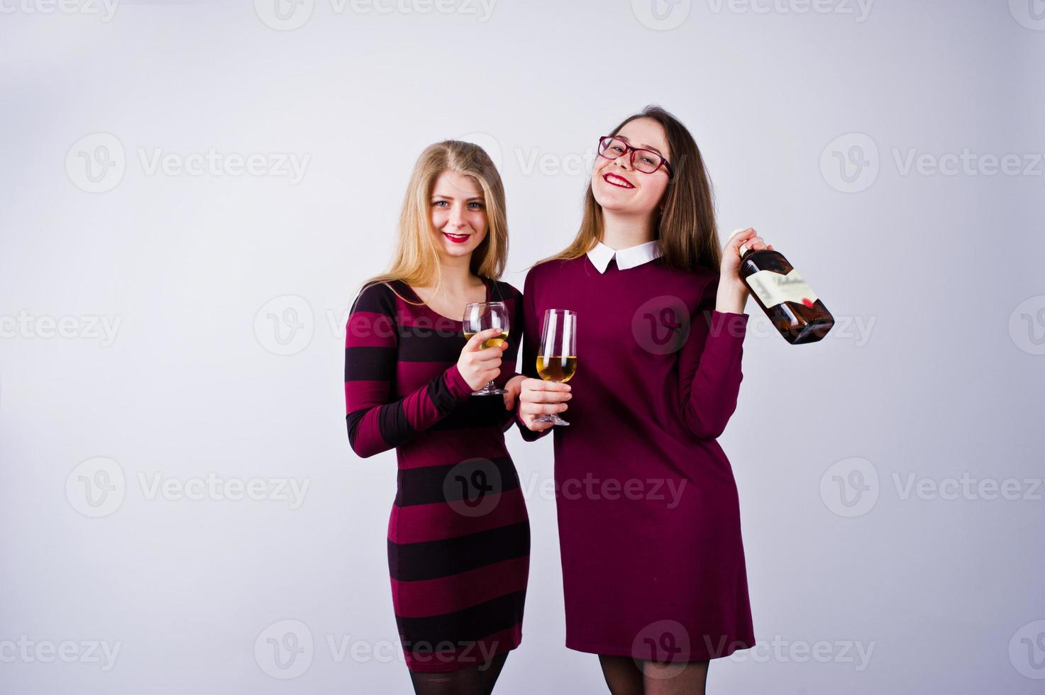 Two attractive friends in purple dresses drink sparkling wine or champagne in the studio. photo