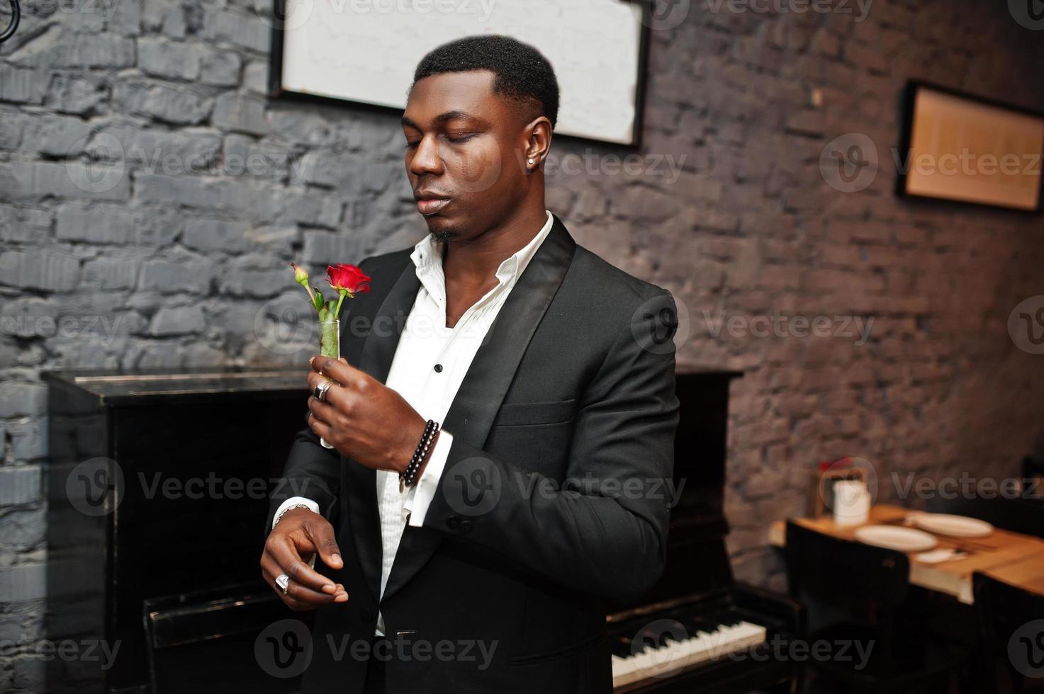 Strong powerful african american man in black suit sniff flower in test tube against piano. photo