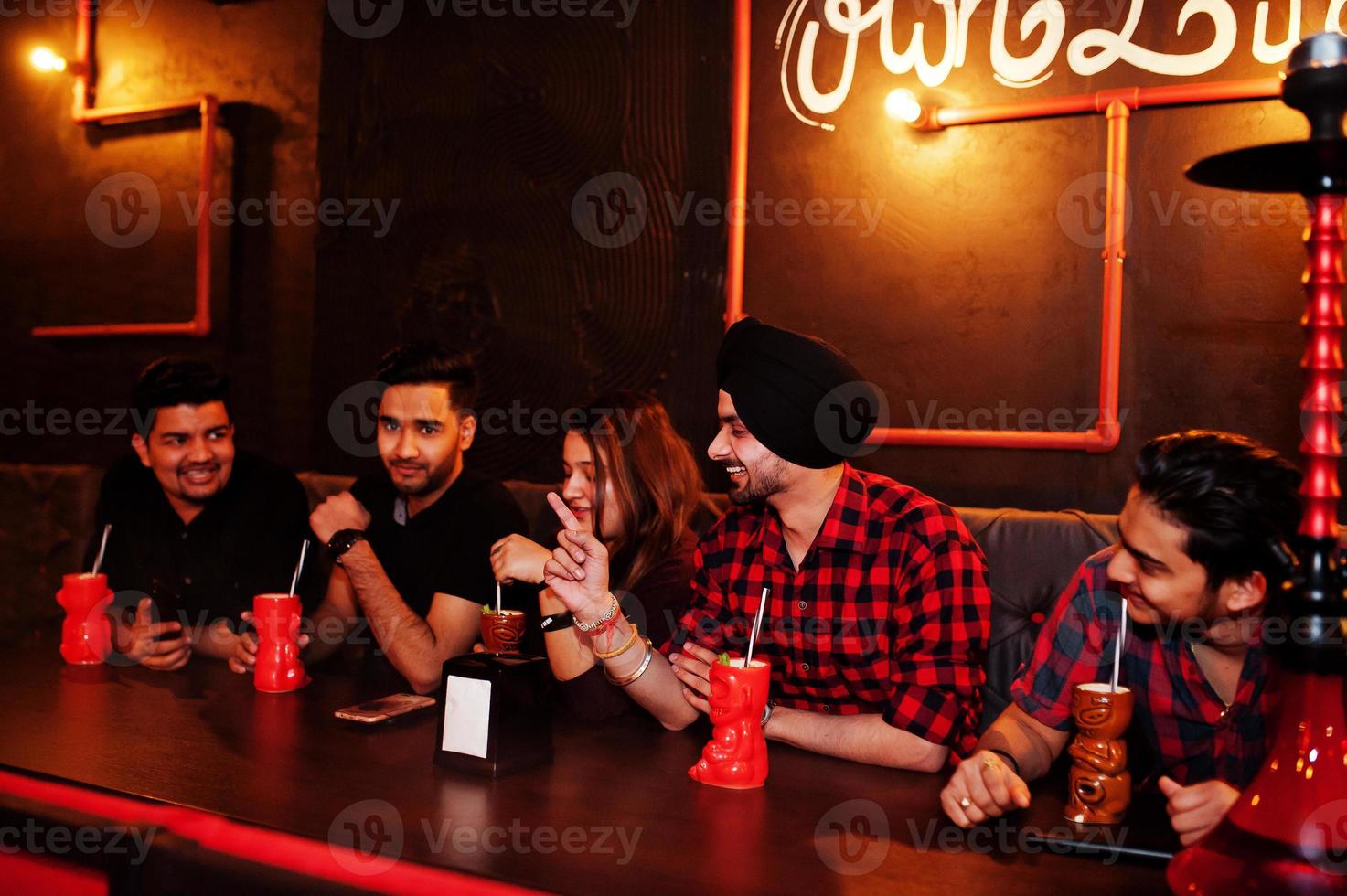 Group of indian friends having fun and rest at night club, drinking cocktails and smoke hookah. photo