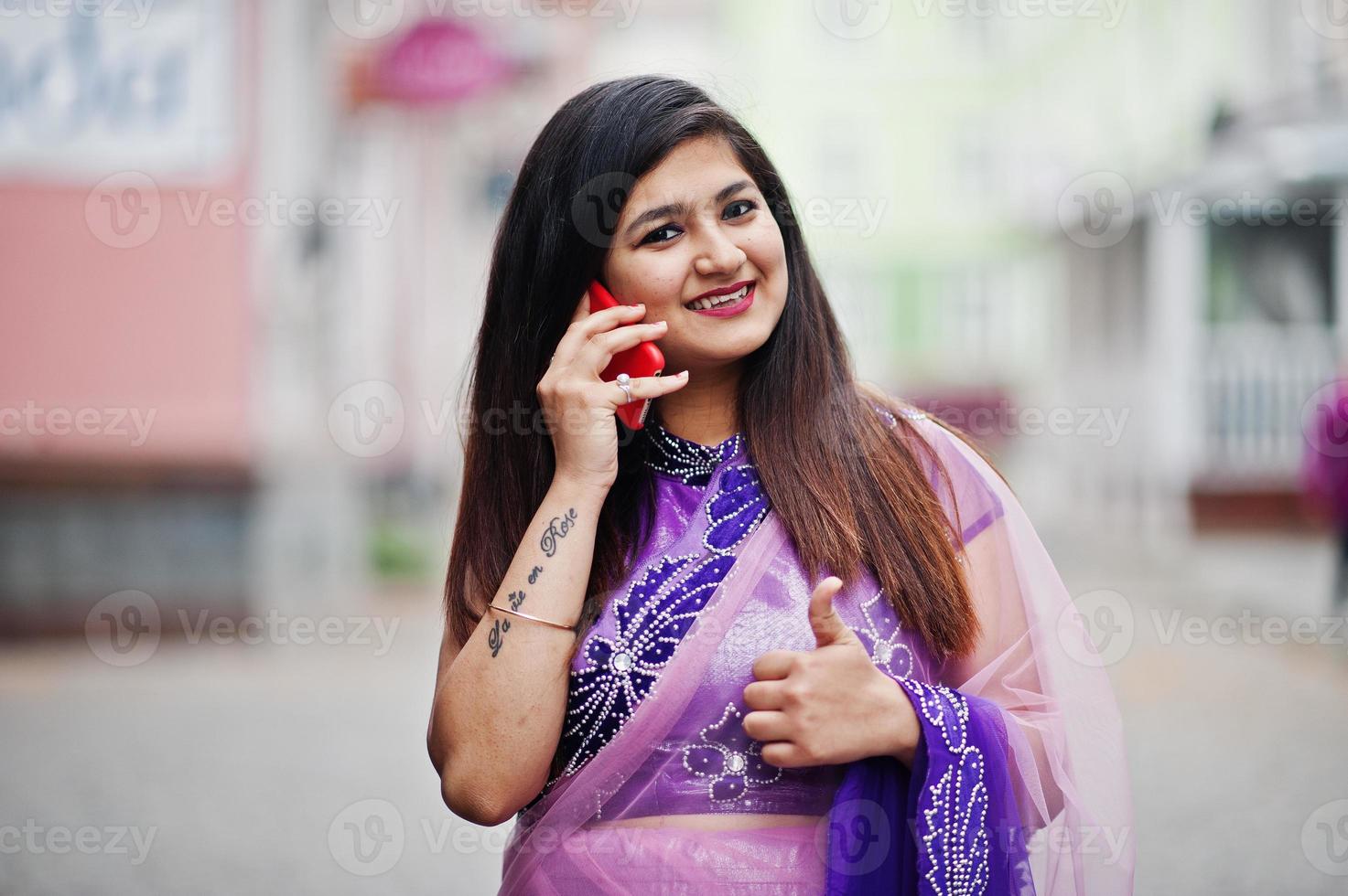 Indian hindu girl at traditional violet saree posed at street and speaking on phone, shows thumb up. photo