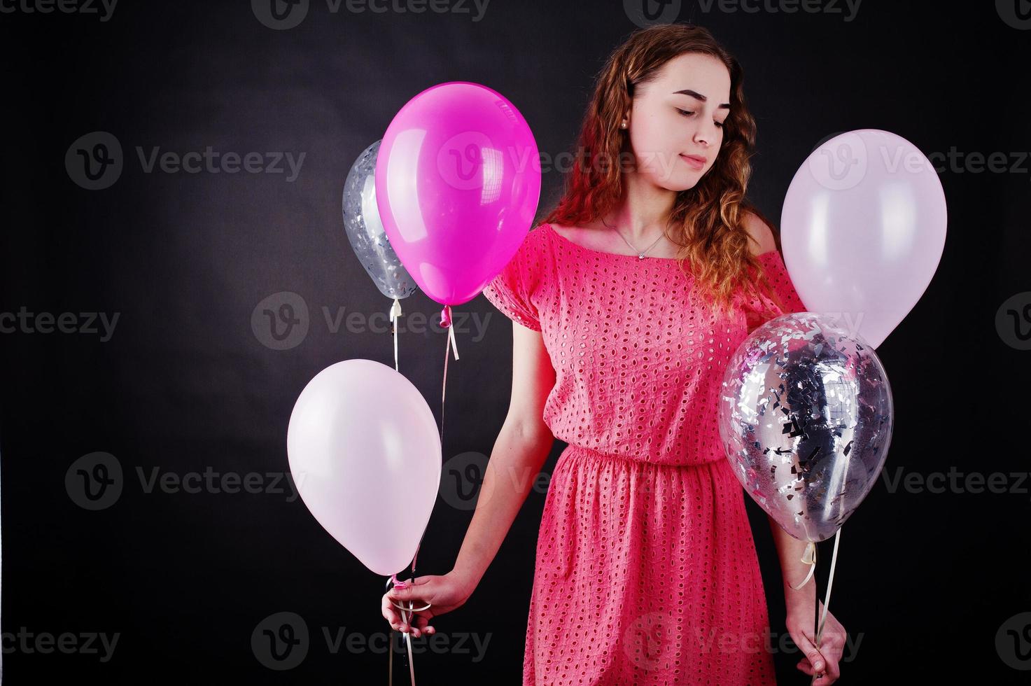 Young girl in red dress with balloons against black background on studio. photo