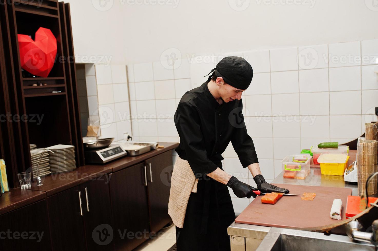 chef profesional vestido de negro haciendo sushi y rollos en la cocina de un restaurante de comida tradicional japonesa. foto